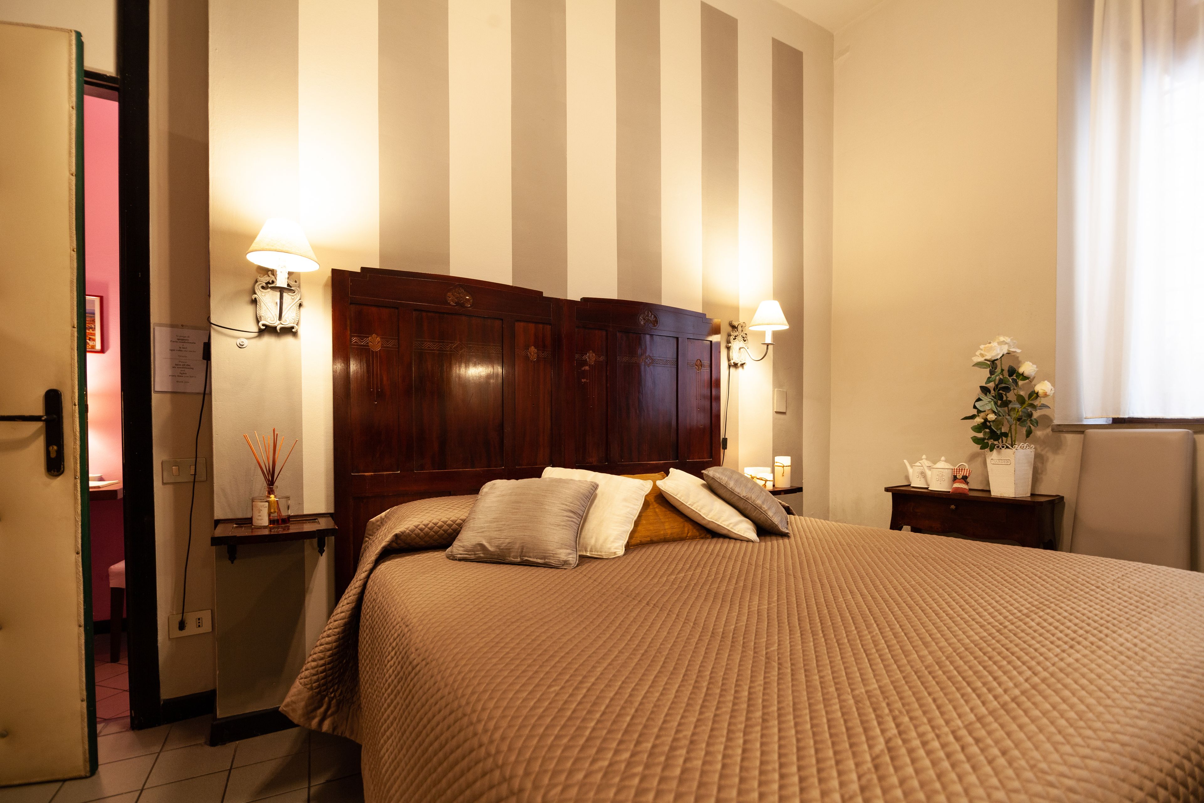 Een hotelkamer met een groot bed, twee bedlampen, een nachtkastje met een bloevas en een houten hoofdbord.