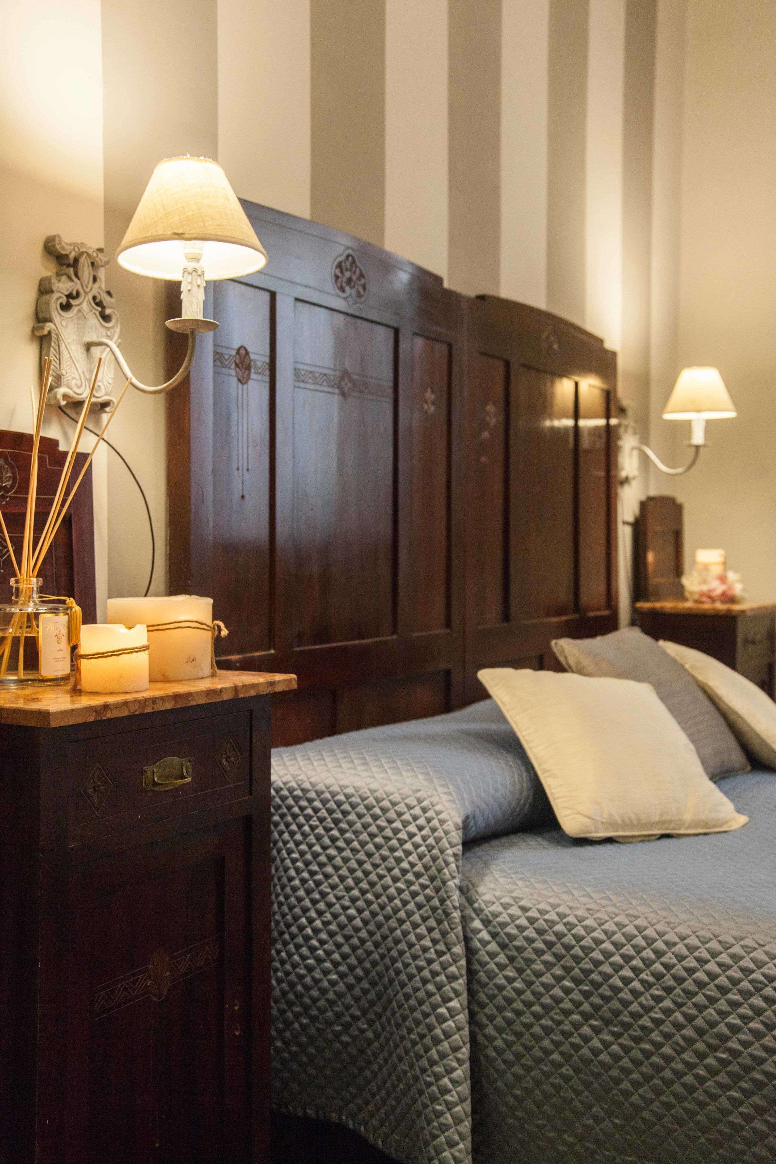 A neatly made bed with a quilted cover, a bedside table with a lamp, and a decorative wall piece.