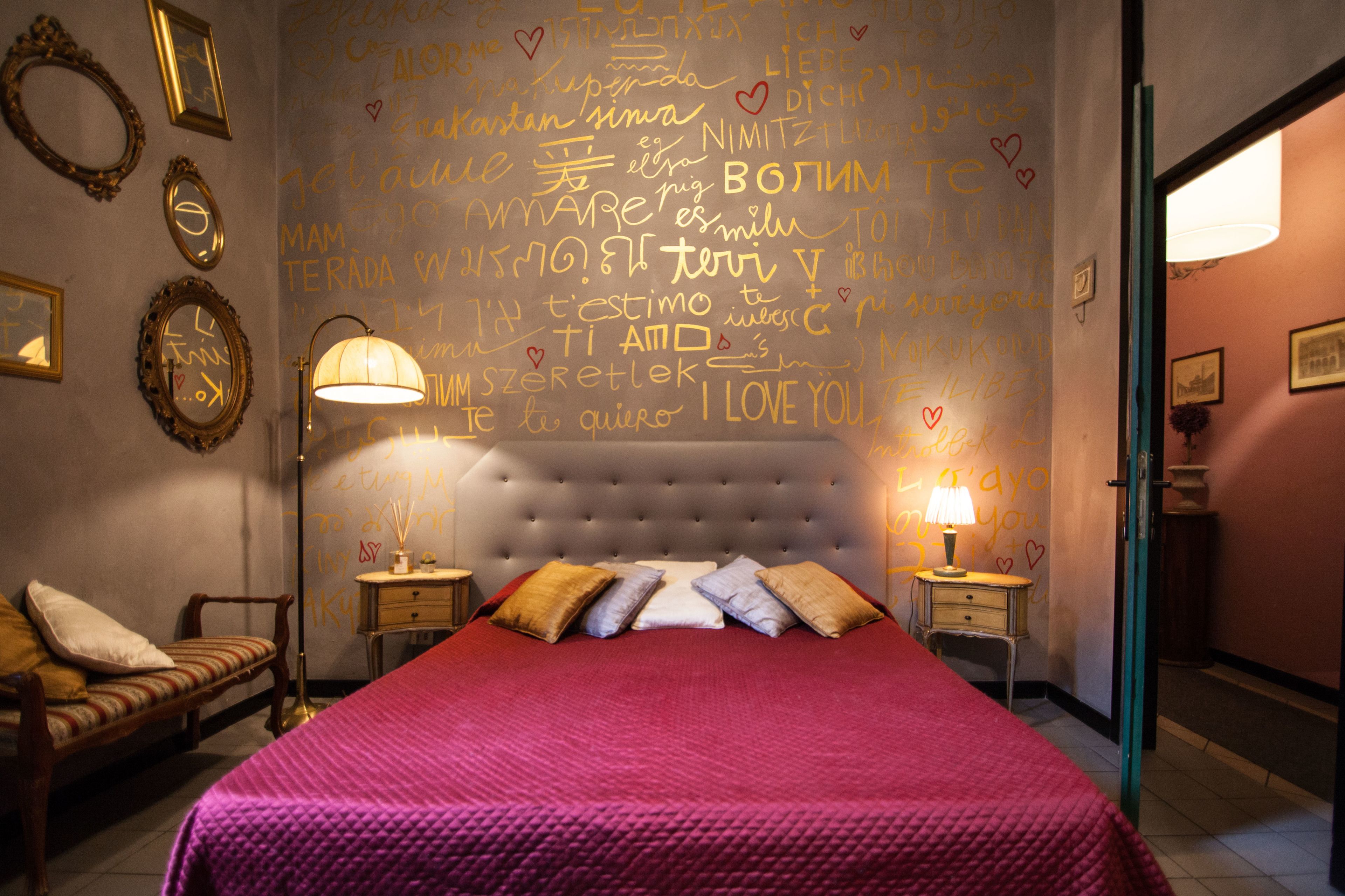 Un dormitorio con una cama grande, dos mesitas de noche, una lámpara y una pared con varias escrituras y dibujos.