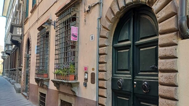 A building with a large arched door, multiple windows with shutters, and a sign indicating rooms for rent. - La Colonna ( Historic Center ) (Lucca)