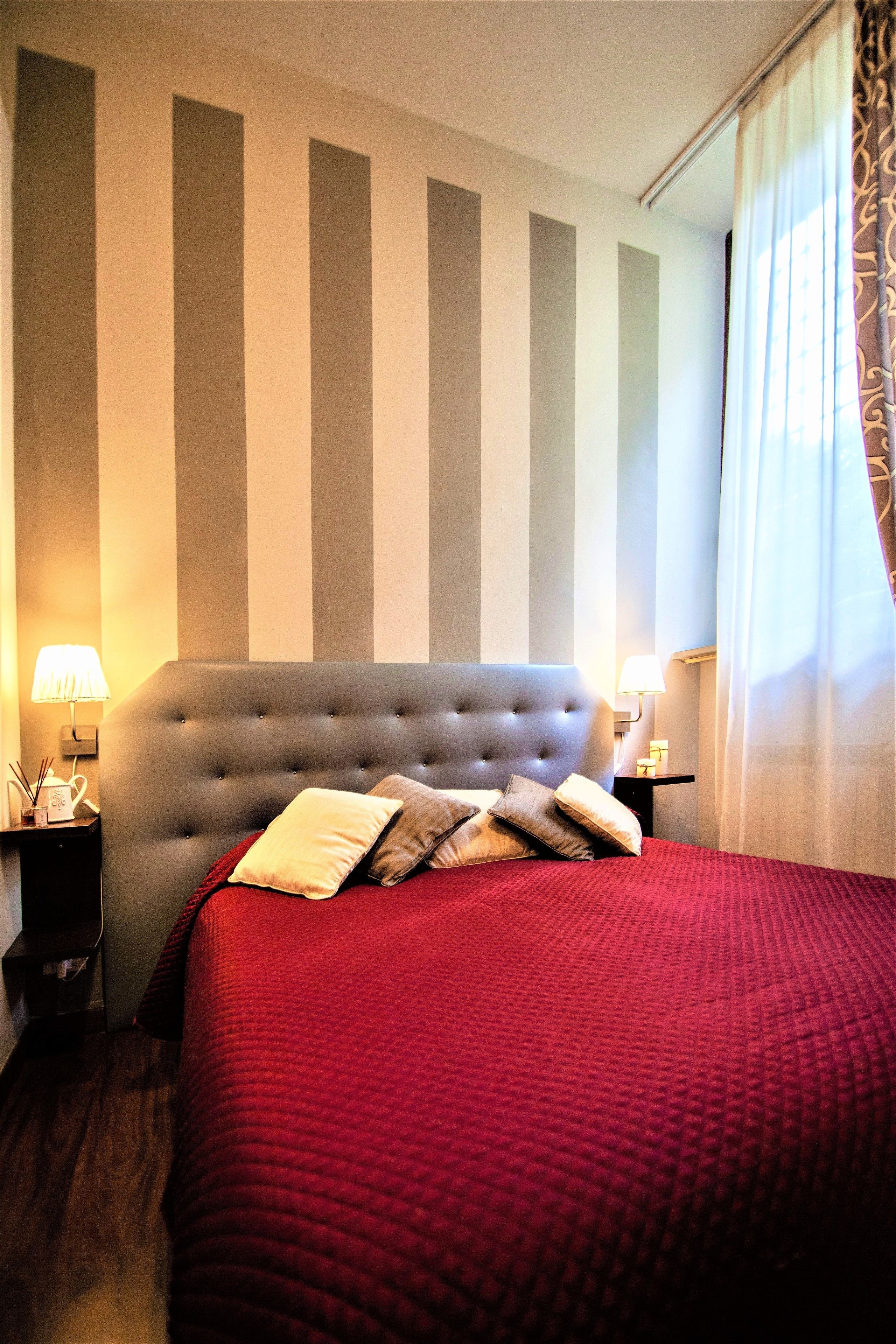 A hotel room with a large bed, striped wall, two bedside tables with lamps, and a window with curtains.