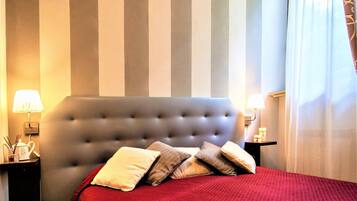 A hotel room with a large bed, striped wall, two bedside tables with lamps, and a window with curtains.