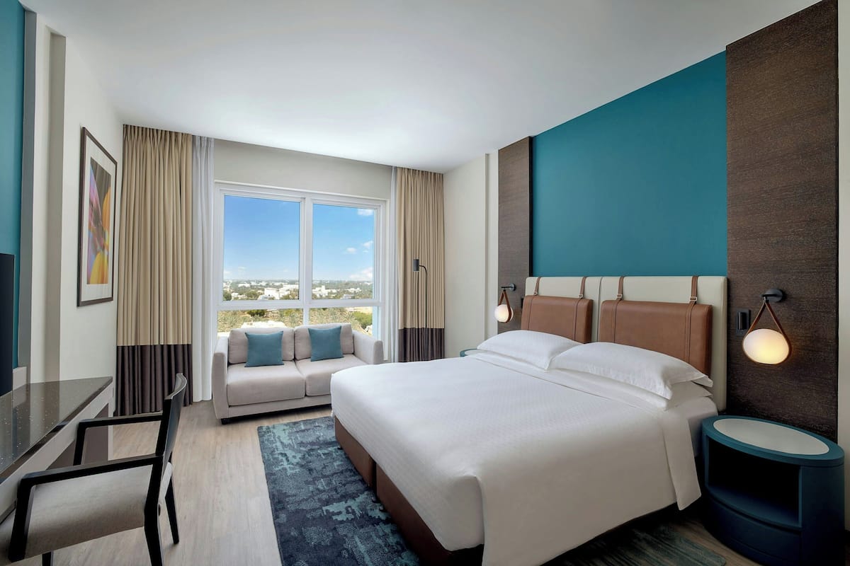 A hotel room with a large bed, a sofa, a dining table, and a view of the city.