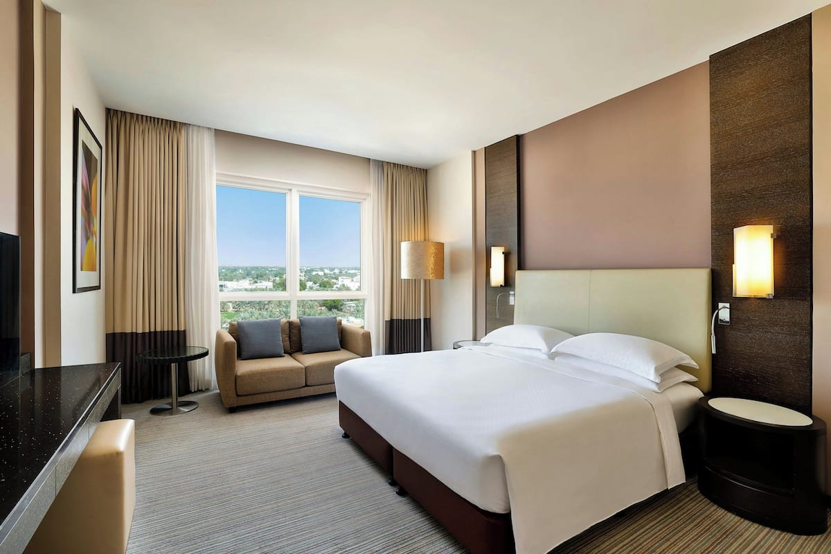 A hotel room with a large bed, a sofa, a desk, and a view of the city.
