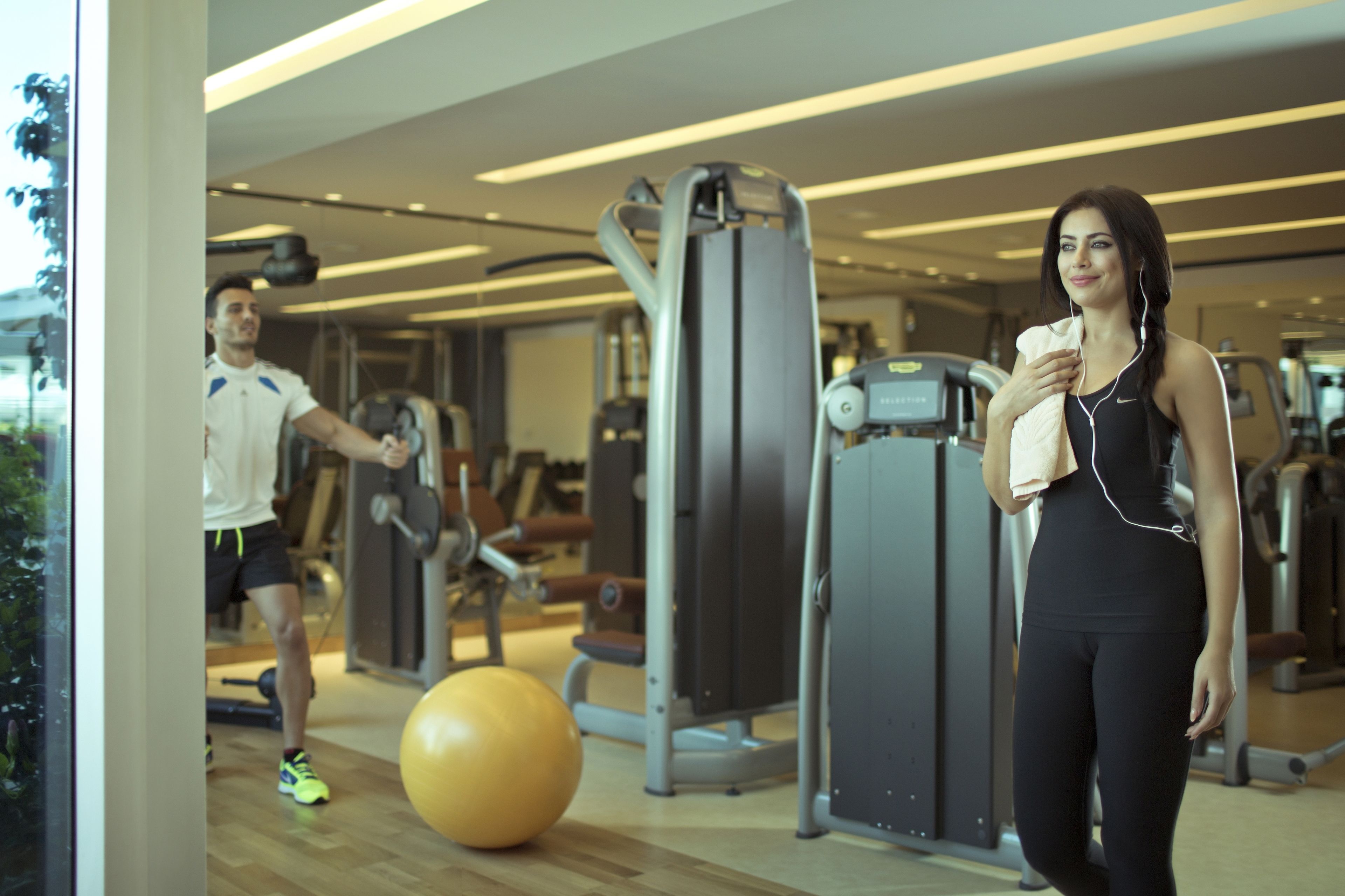 Een sportschool met trainingsapparatuur, een grote fitnessbal en iemand met een handdoek.