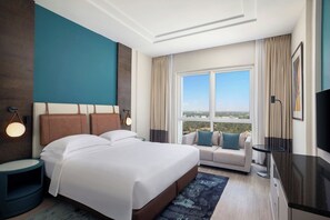 Habitación de hotel con una cama grande, un sofá, un televisor y una ventana con vistas a la ciudad.