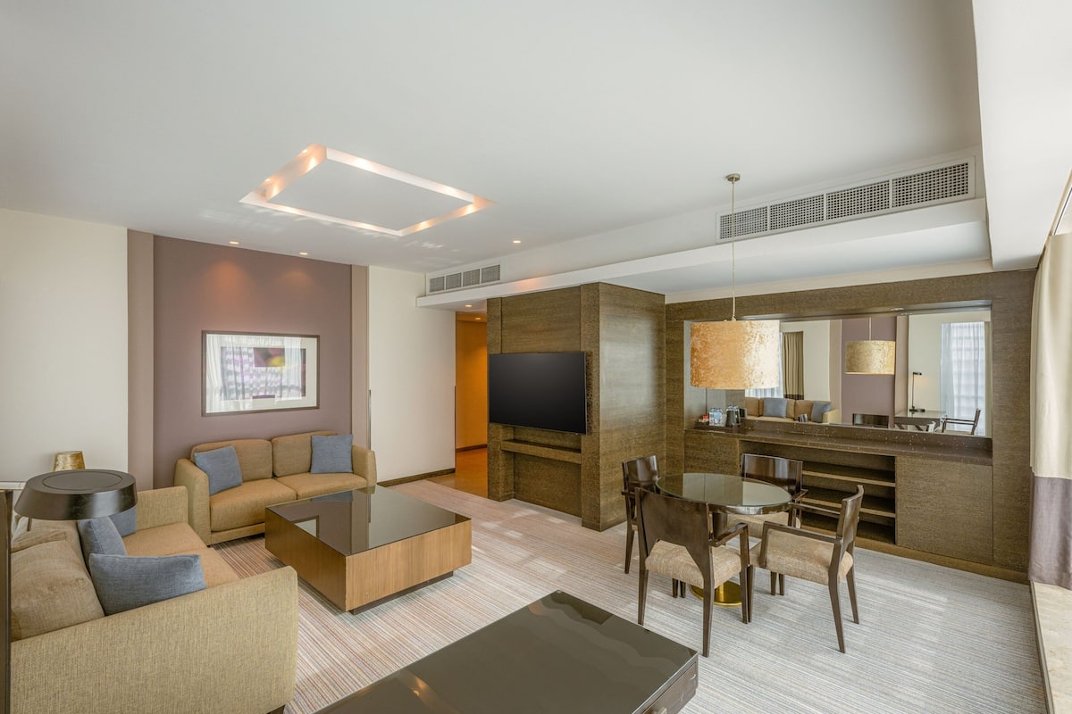 A modern hotel room with a living area, a dining table, and a TV.