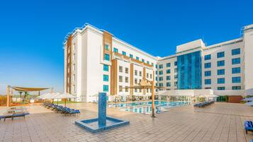 Un hotel con piscina, sillones de descanso y sombrillas.