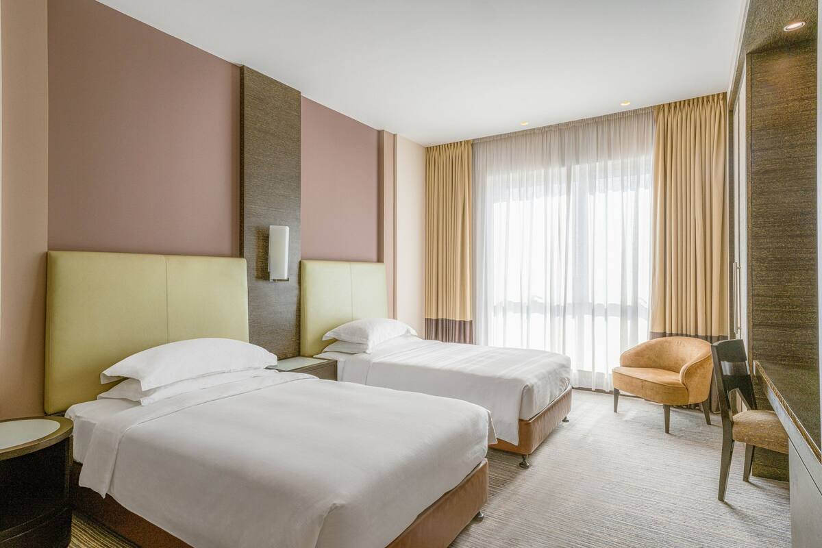 A hotel room with two beds, a sofa, a chair, and a large window with curtains.