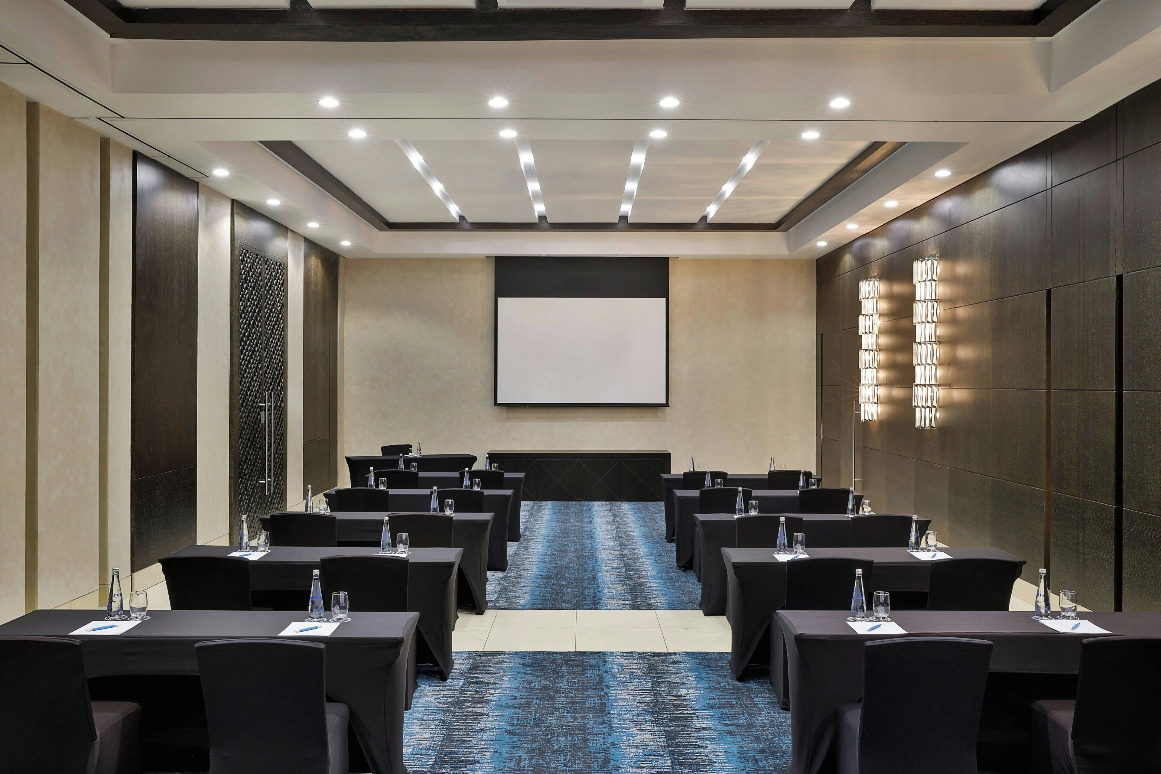 A conference room with tables, chairs, a projector screen, and a carpeted floor.