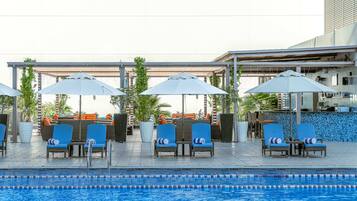 A poolside area with lounge chairs and umbrellas, a tiled floor, and a pool with lane dividers.
