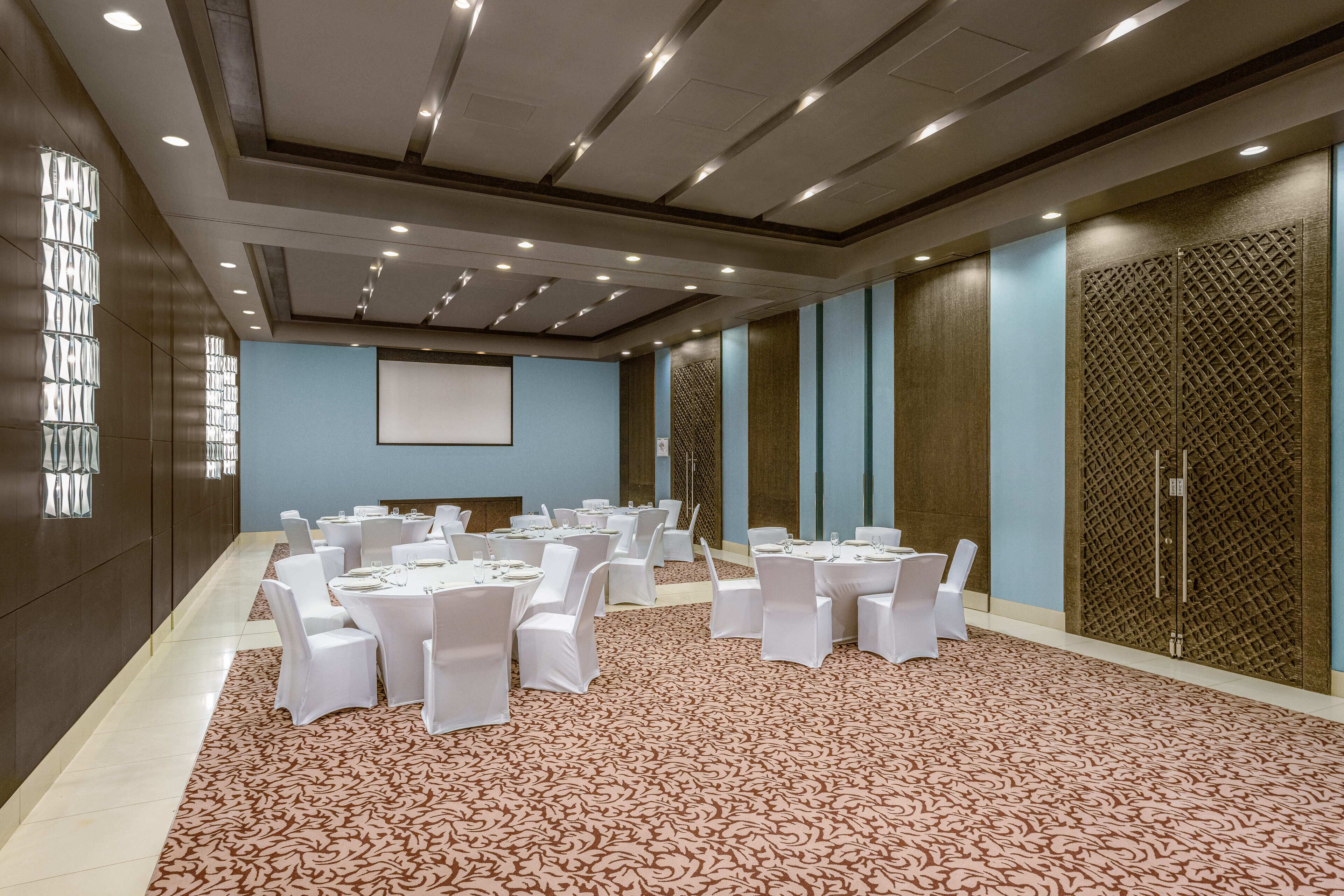 A conference room with multiple tables and chairs, a projector screen, and a patterned carpet.