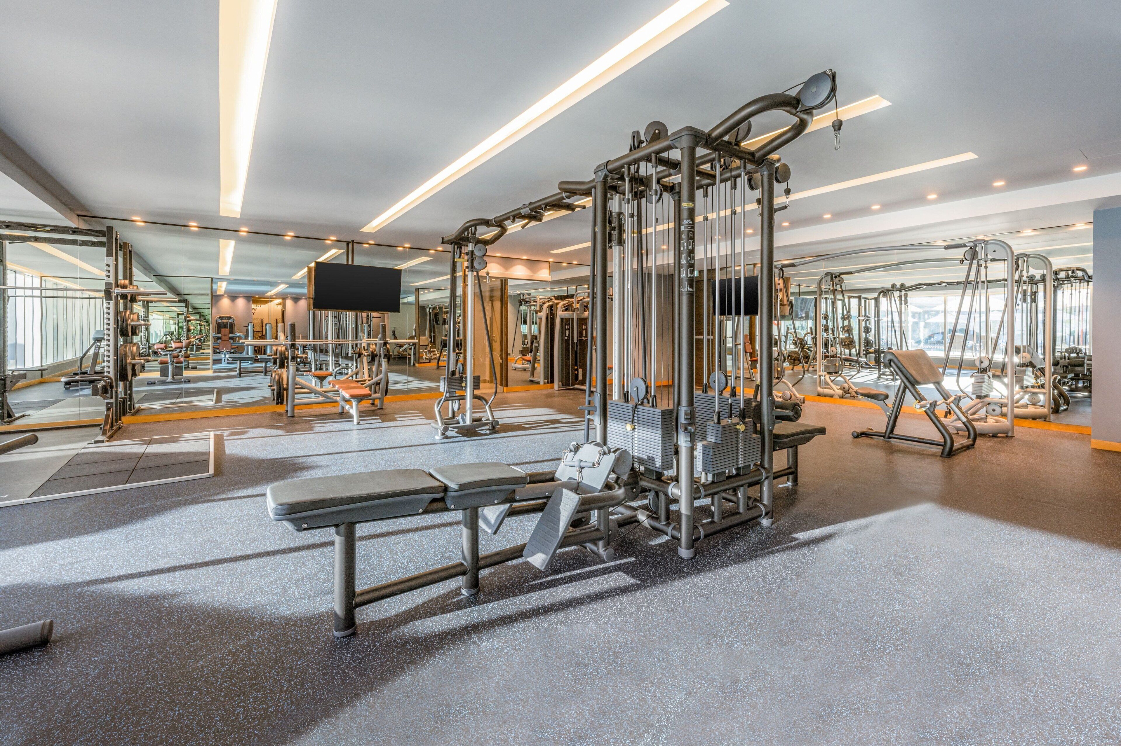 Une salle de sport moderne équipée de divers appareils d’exercice, de miroirs et d’un téléviseur à écran plat.