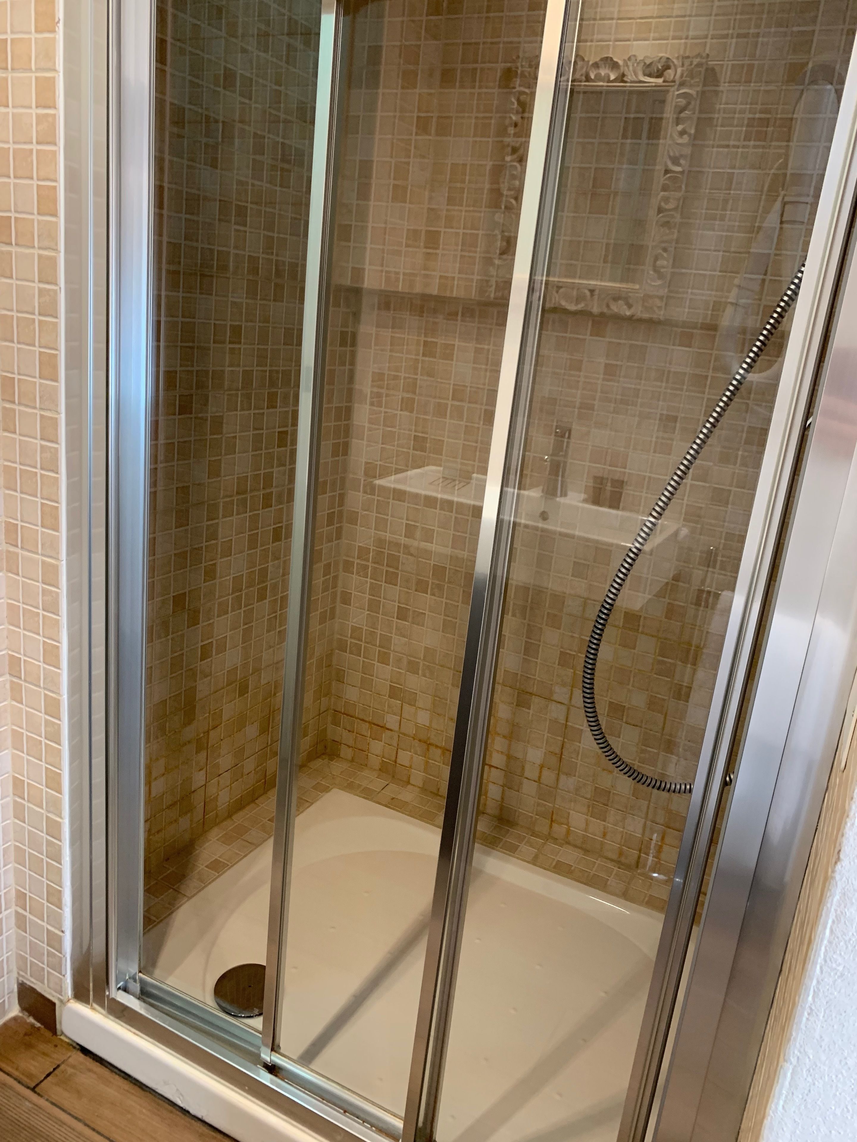 A glass-enclosed shower with beige mosaic tiles and a handheld showerhead.