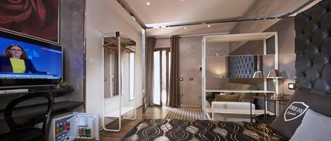 A modern hotel room with a bed, a TV, a wardrobe, and a seating area.