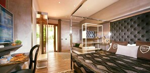 A modern hotel room with a bed, a desk with a laptop, a TV, and a balcony with a view.