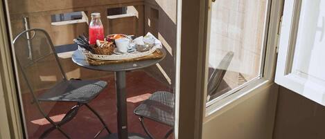 A small balcony with a table set for breakfast, including a basket of bread, a bottle of juice, and a cup.
