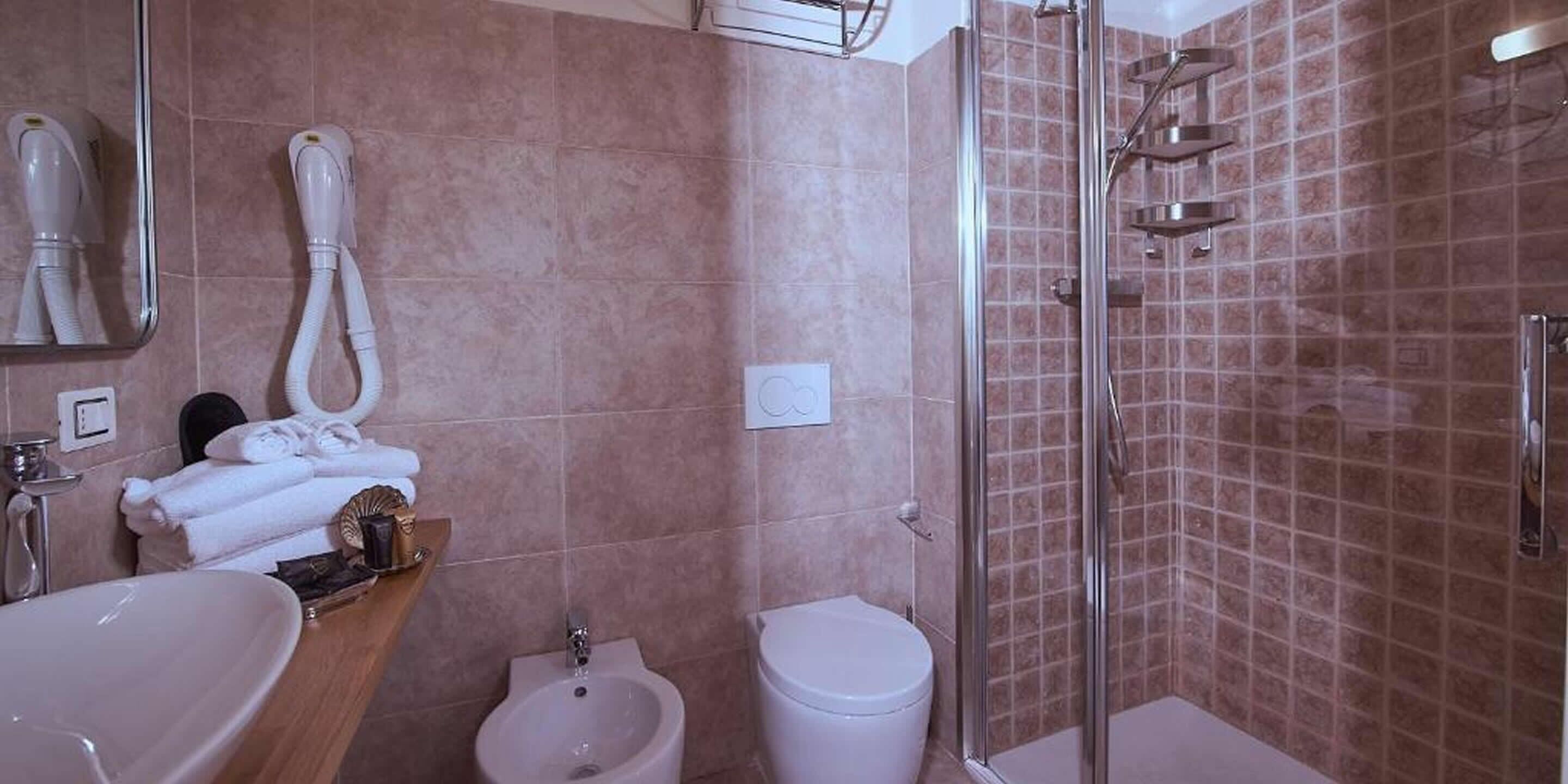 Un baño con lavabo, bidé, inodoro y cabina de ducha con mampara de cristal.