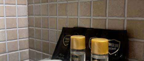 Una encimera de baño con artículos de aseo, incluyendo una botella de champú, una botella de acondicionador y una bolsa de discos de algodón, todo con la marca 'Tower Inn Hotels'.
