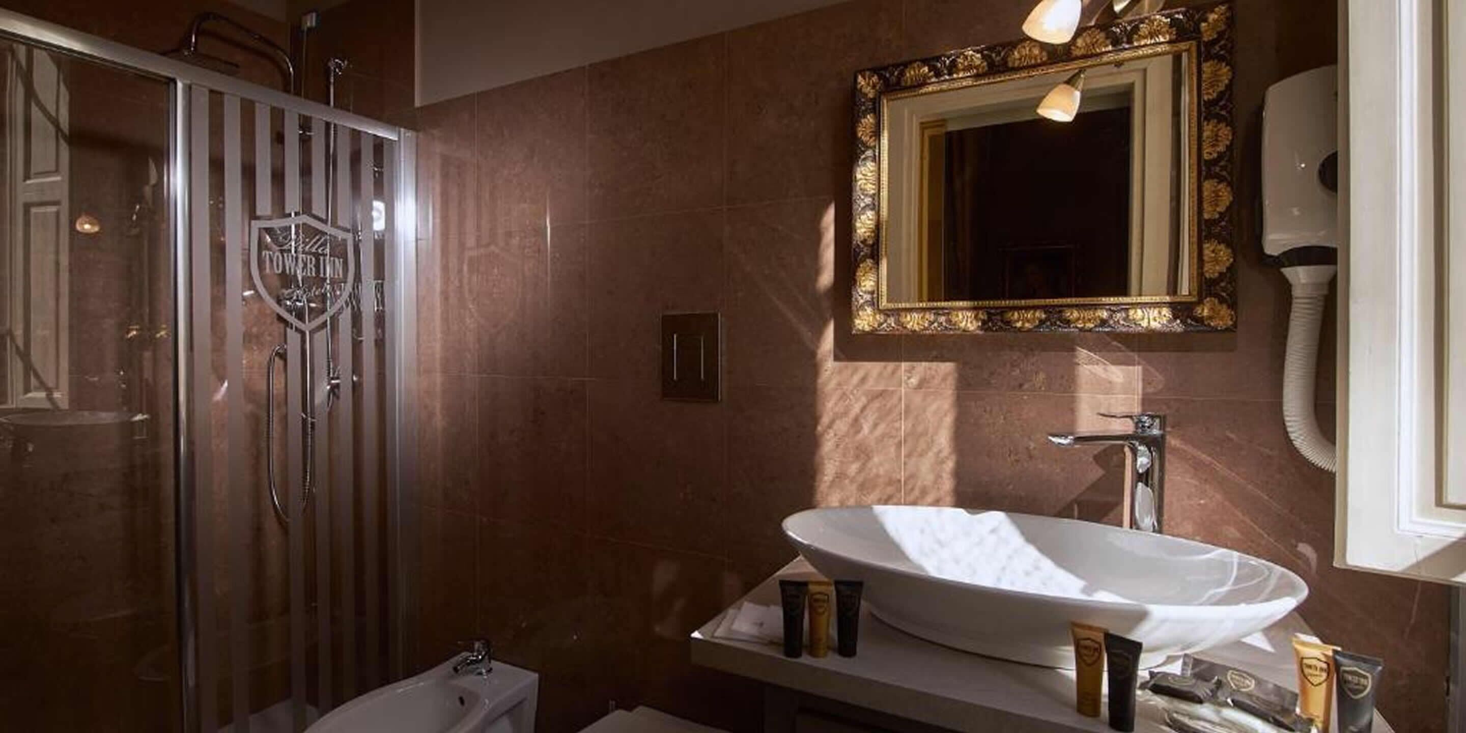Un baño con un lavamanos ovalado grande, cabina de ducha con mampara de vidrio y un espejo con marco dorado.