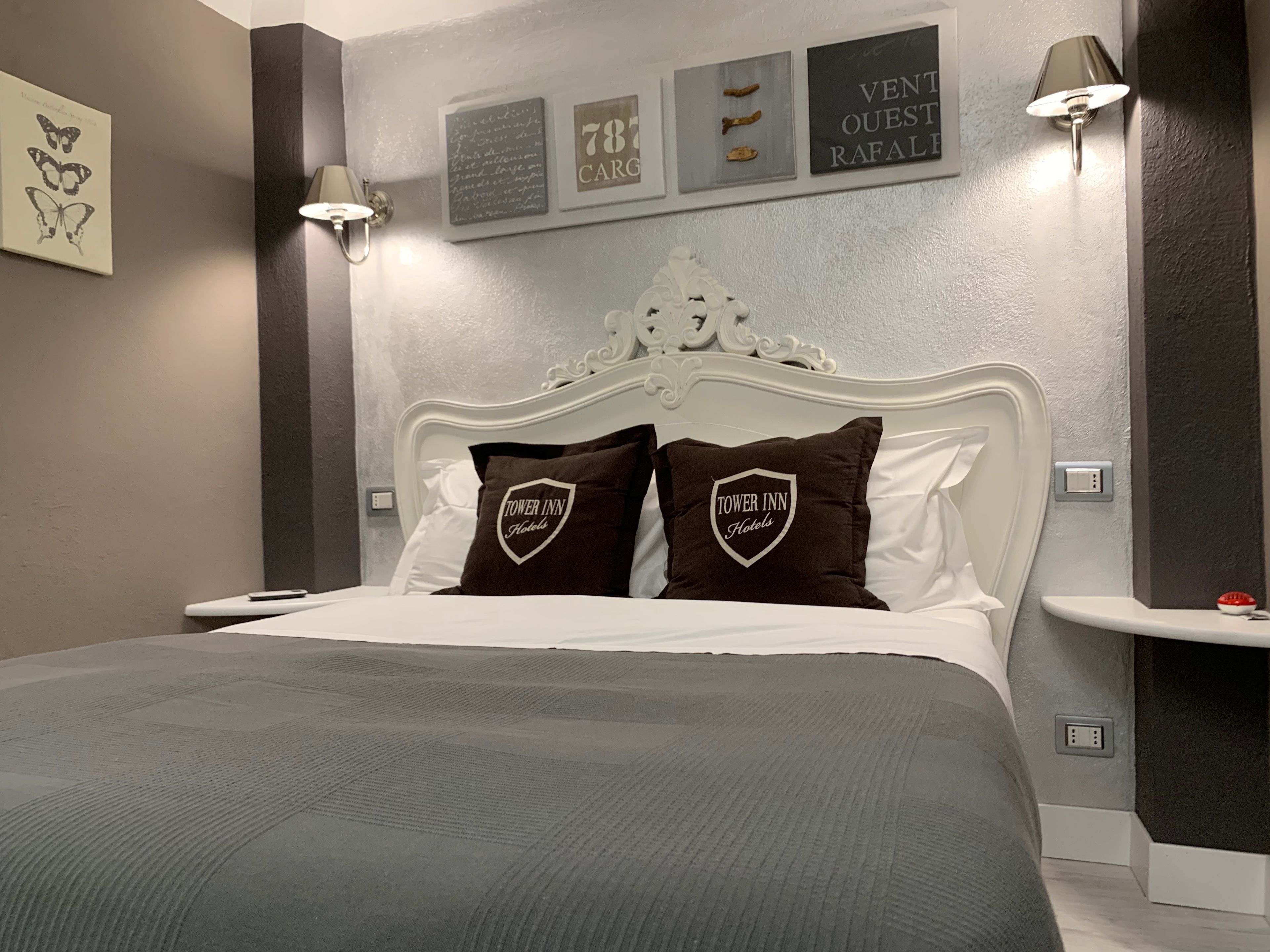 A hotel room with a white headboard, two pillows with the hotel logo, a bedside table, and wall-mounted artwork.