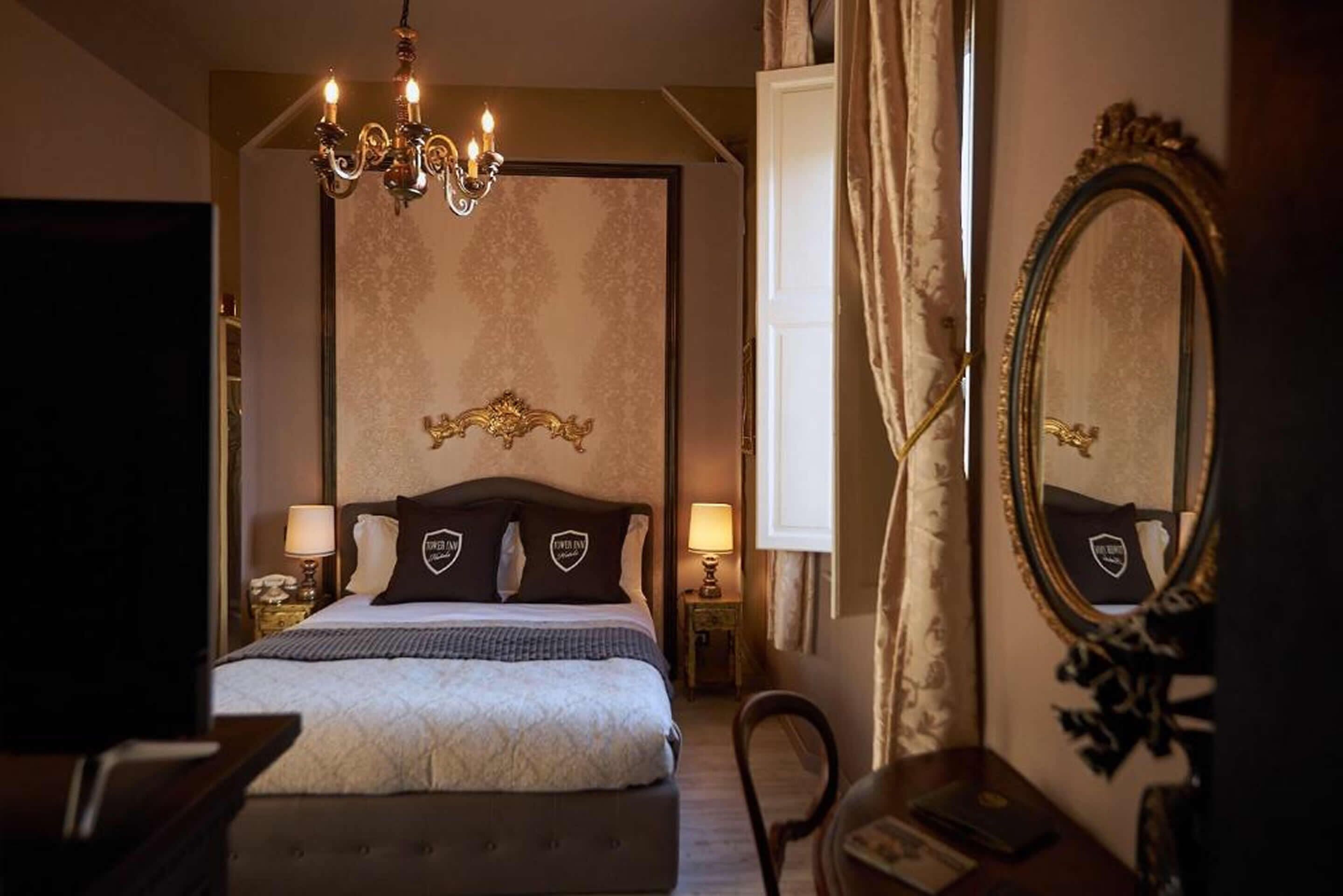 Une chambre d’hôtel avec un grand lit, un lustre, un miroir et un bureau avec une chaise.