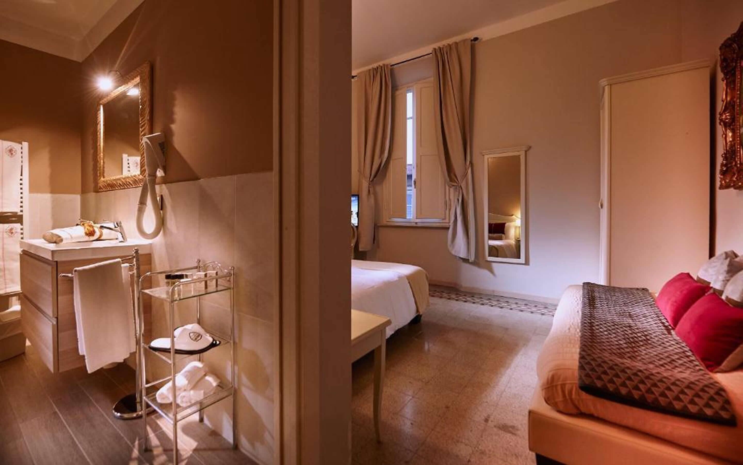 A hotel room with a bathroom, a bed, a sofa, and a mirror.