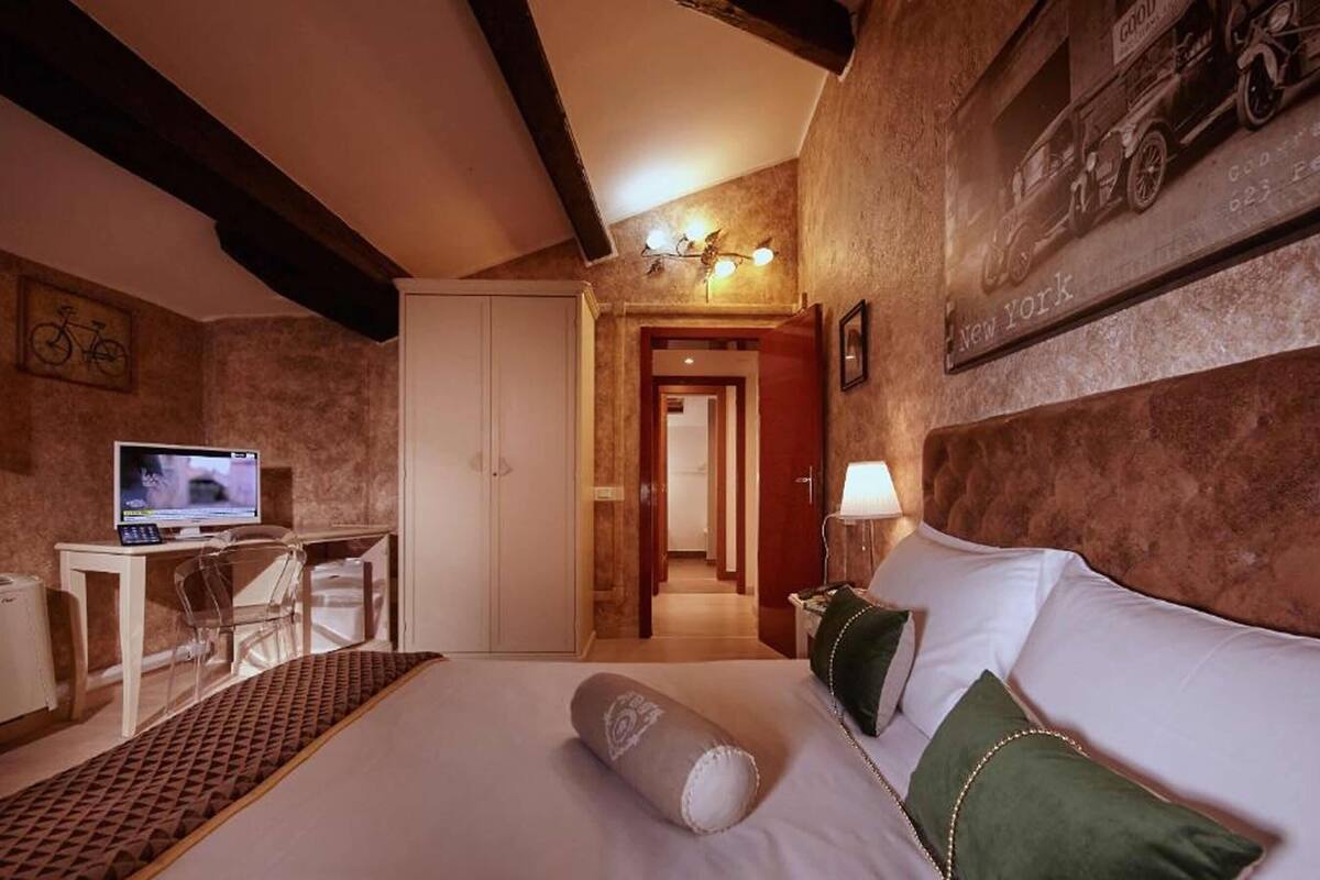 Una habitación de hotel con una cama, un escritorio con ordenador, una lámpara y una obra de arte colgada en la pared.