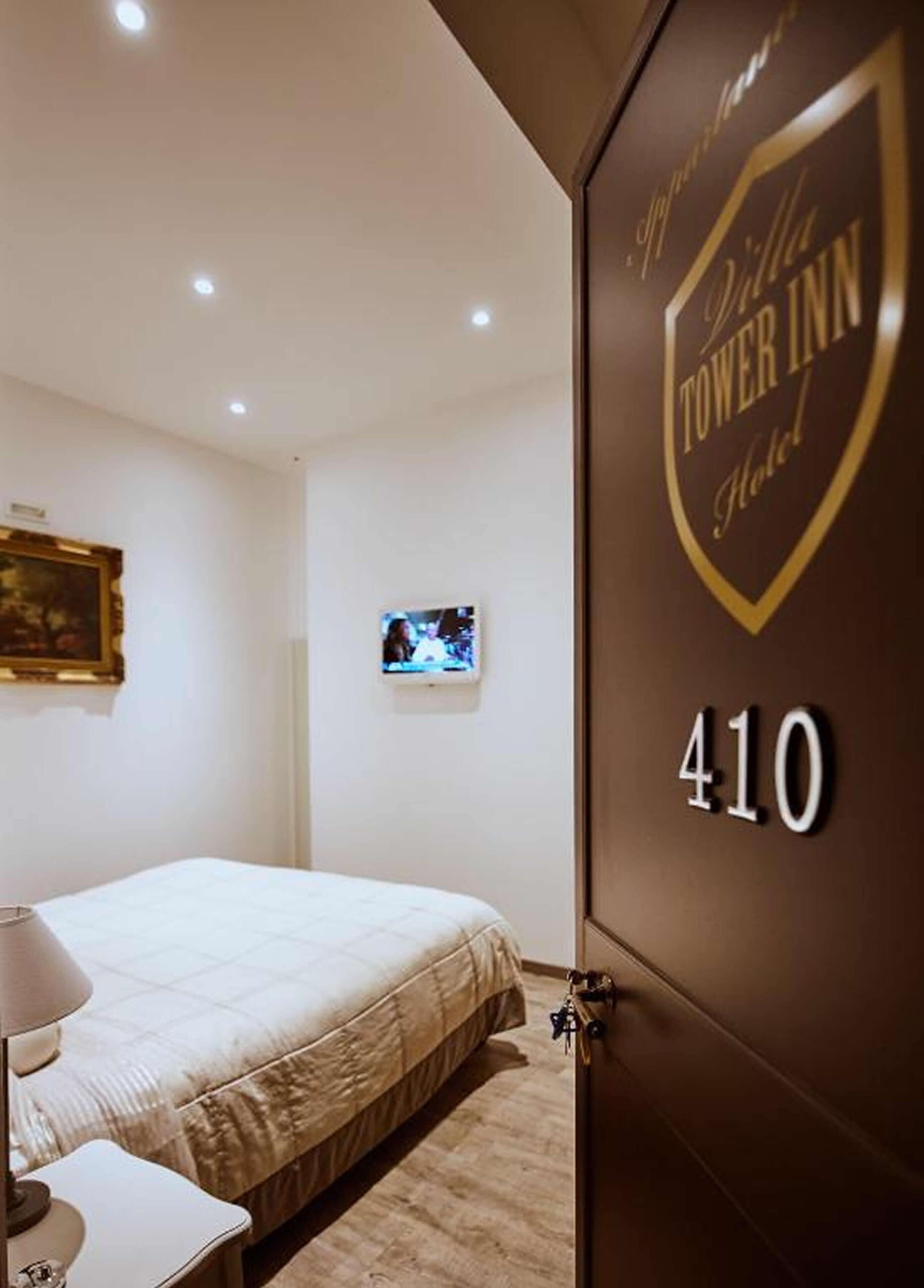 Quarto de hotel com cama, televisão e porta com o nome do hotel e número do quarto.