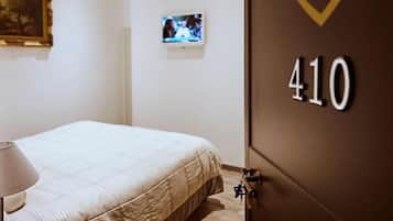 Quarto de hotel com cama, televisão e porta com o nome do hotel e número do quarto.