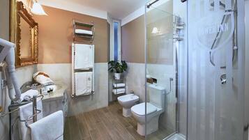 A modern bathroom with a glass shower enclosure, a toilet, bidet, and a sink with a towel rack.