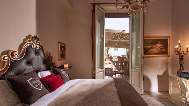 A luxurious bedroom with a large bed, a chandelier, and a view of an outdoor terrace. - Villa Tower Inn (Pisa)