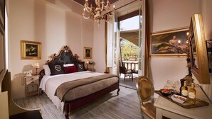 A bedroom with a large bed, a chandelier, a desk with a tray of items, and a painting on the wall. - Villa Tower Inn (Pisa)