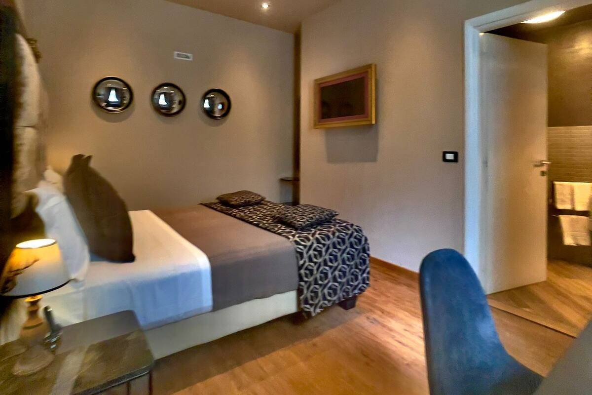 Un dormitorio moderno con cama, mesita de noche y una silla. Hay luces empotradas en la pared y un equipo de aire acondicionado.