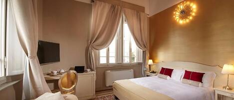 A hotel room with a bed, bedside tables, a desk, a chair, a TV, and a window with curtains.