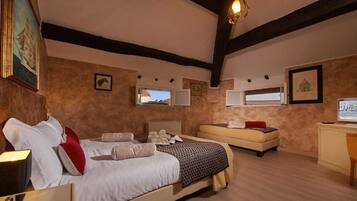 A bedroom with a large bed, a smaller sofa, a desk, and a computer.