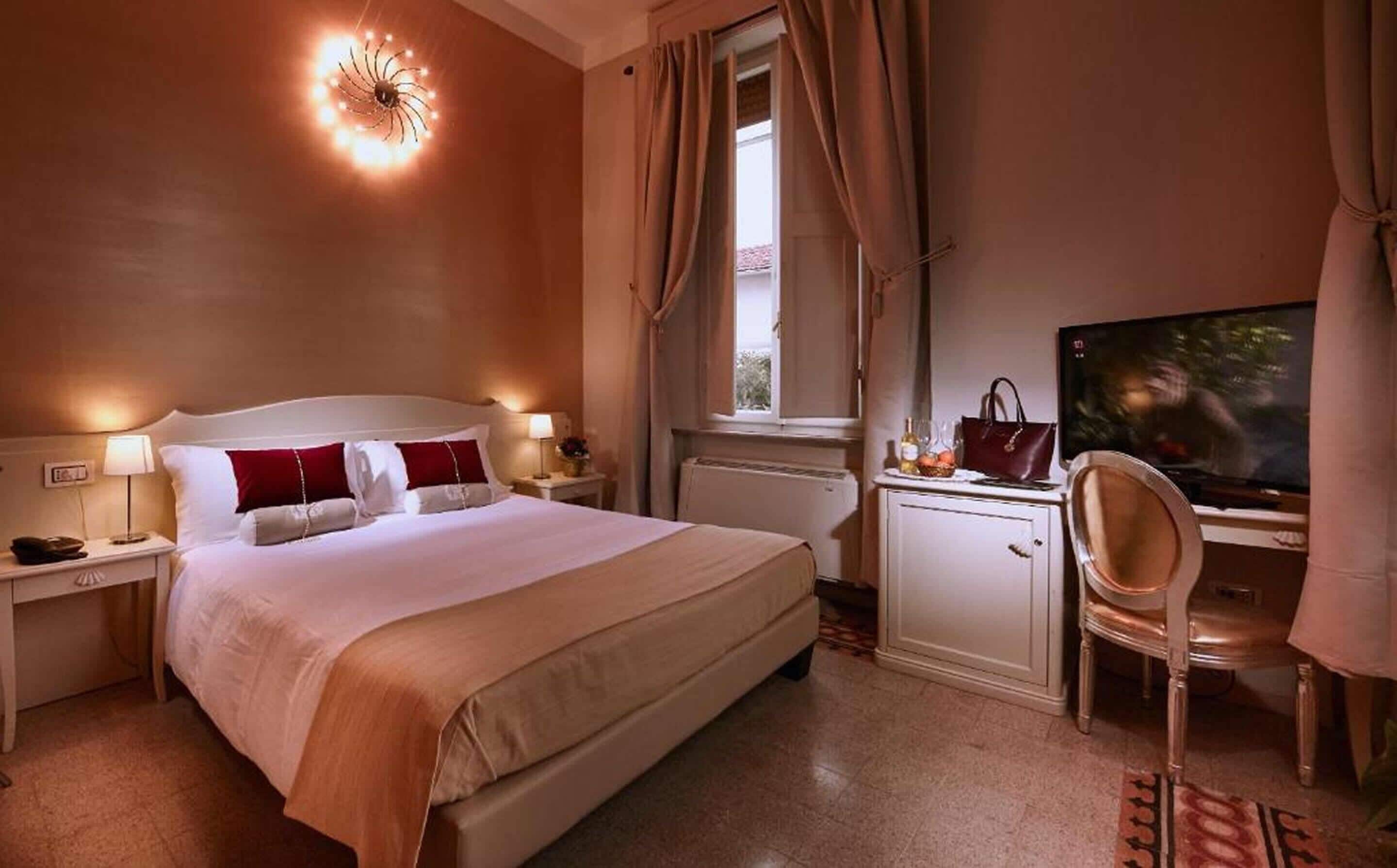 A hotel room with a bed, bedside tables, a desk with a chair, a television, and a window with curtains.