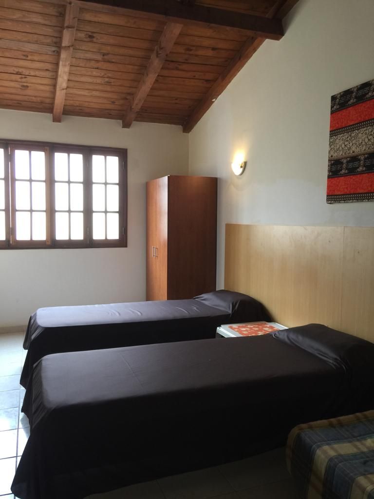 A room with two beds, a wardrobe, and a wall-mounted light fixture.