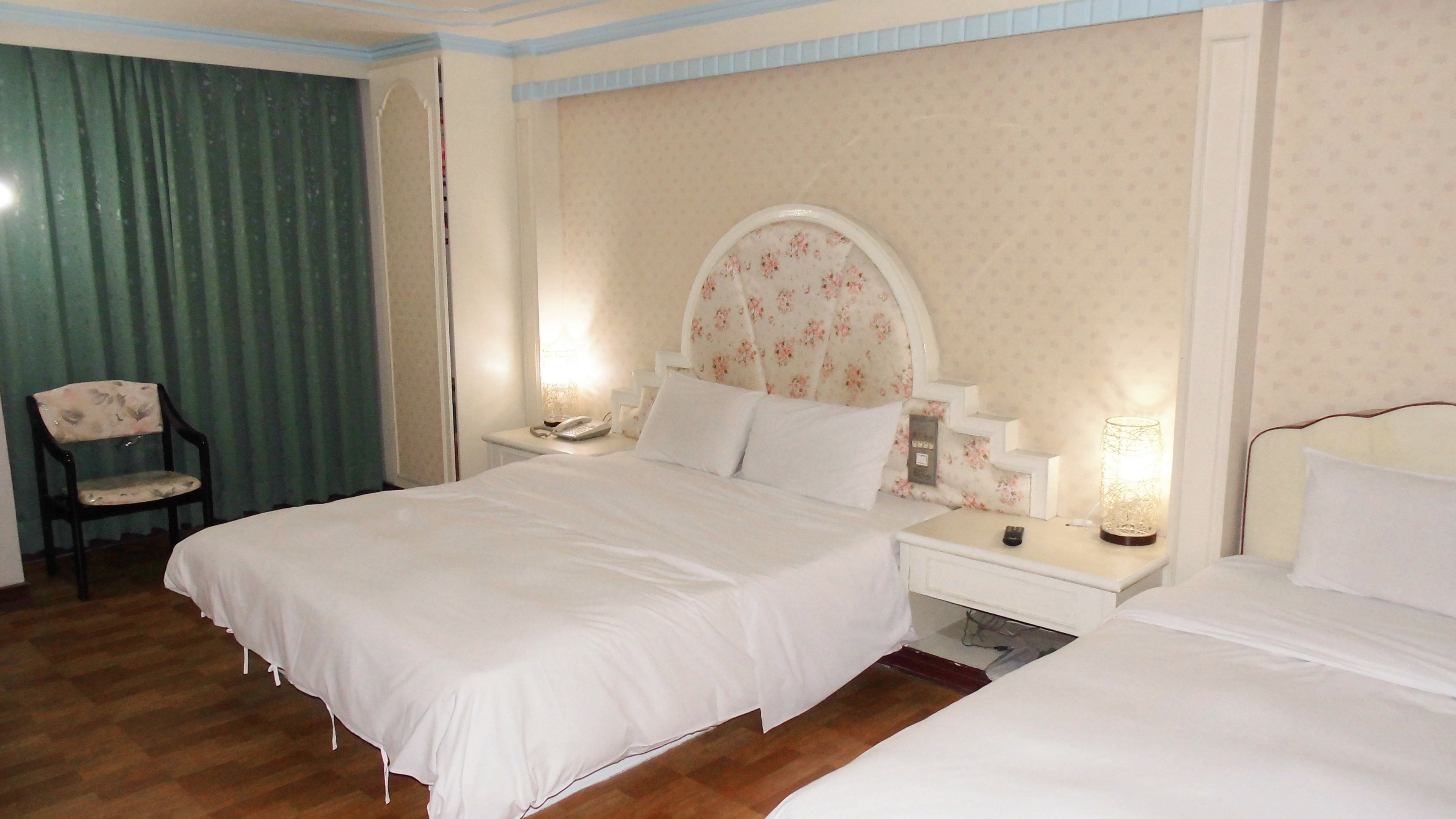 A hotel room with a large bed, a bedside table with a lamp, a chair, and a nightstand with a phone.