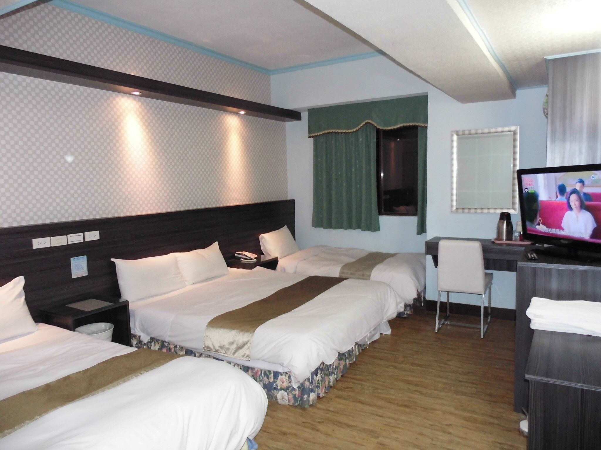 Ett hotellrum med två sängar, ett skrivbord, en TV och ett fönster med gardiner.