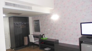 A hotel room with a dark wood floor, a grey sofa, a TV, a small fridge, a mirror, and a wardrobe with a hanging rack. - Modern Plaza Hotel (Kaohsiung)