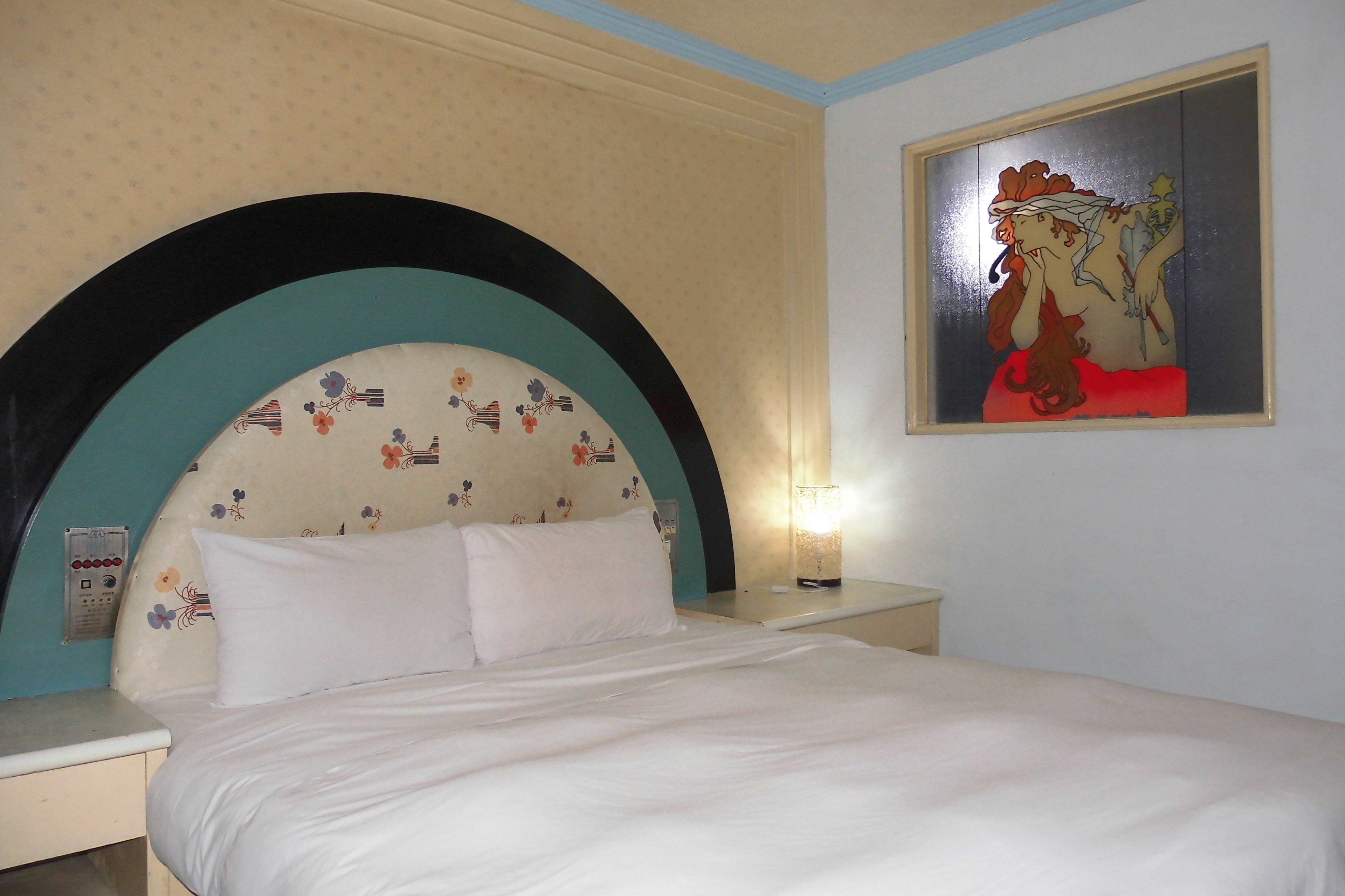 Quarto de hotel com cama, mesa de cabeceira, quadro na parede e tomada.