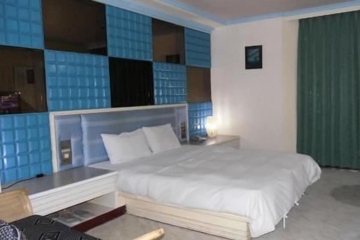 A hotel room with a bed, a television, and a window with blue-tiled walls.