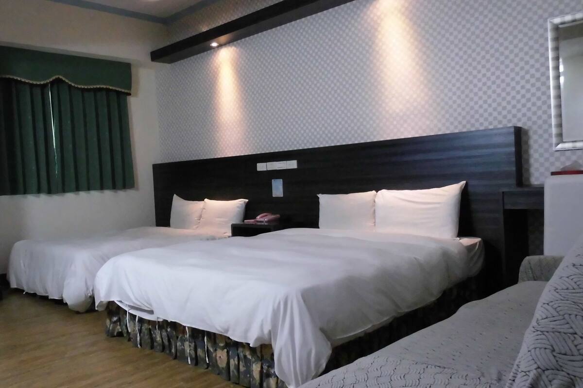 Habitación de hotel con dos camas, suelo de madera, cortina verde y pared con diseño.