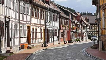 En brostensbelagt gade med bindingsværkshuse, en hvid varevogn parkeret langsiden, og en klar himmel.