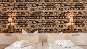 Habitación de hotel con pared de piedra, dos camas con ropa blanca y dos lámparas de noche.
