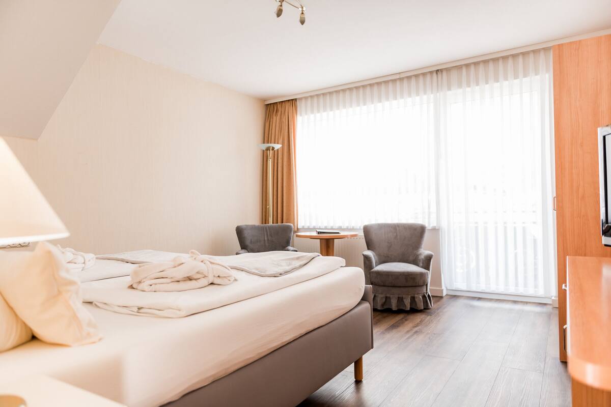 A hotel room with a bed, two armchairs, a small table, and a TV.