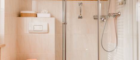 A bathroom with a glass shower enclosure, a toilet with a towel, and a soap dispenser on the wall.