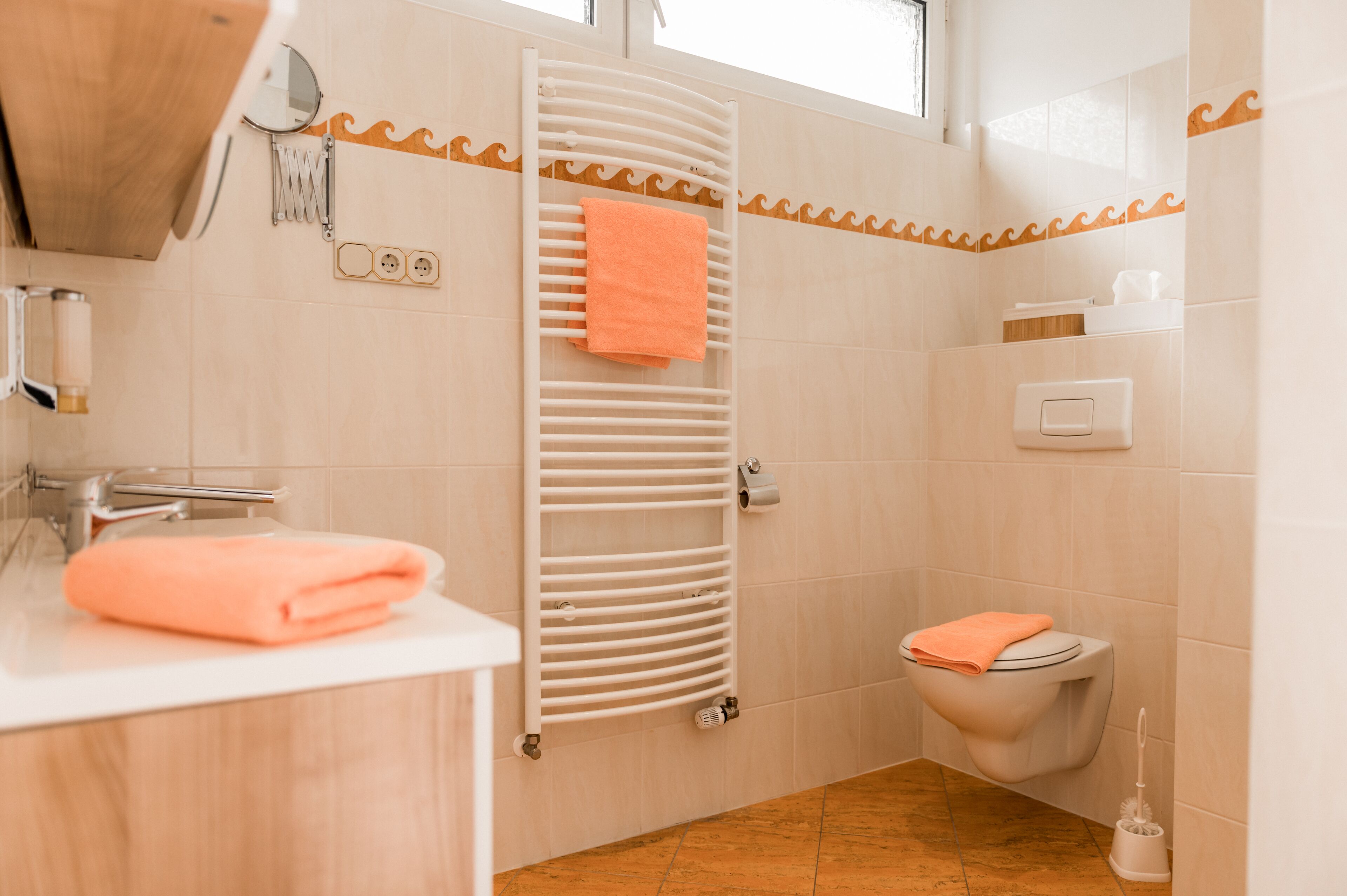 Een badkamer met een witte wastafel, een handdoekhouder met een oranje handdoek, een toilet en een douchegedeelte met een witte handdoekhouder.