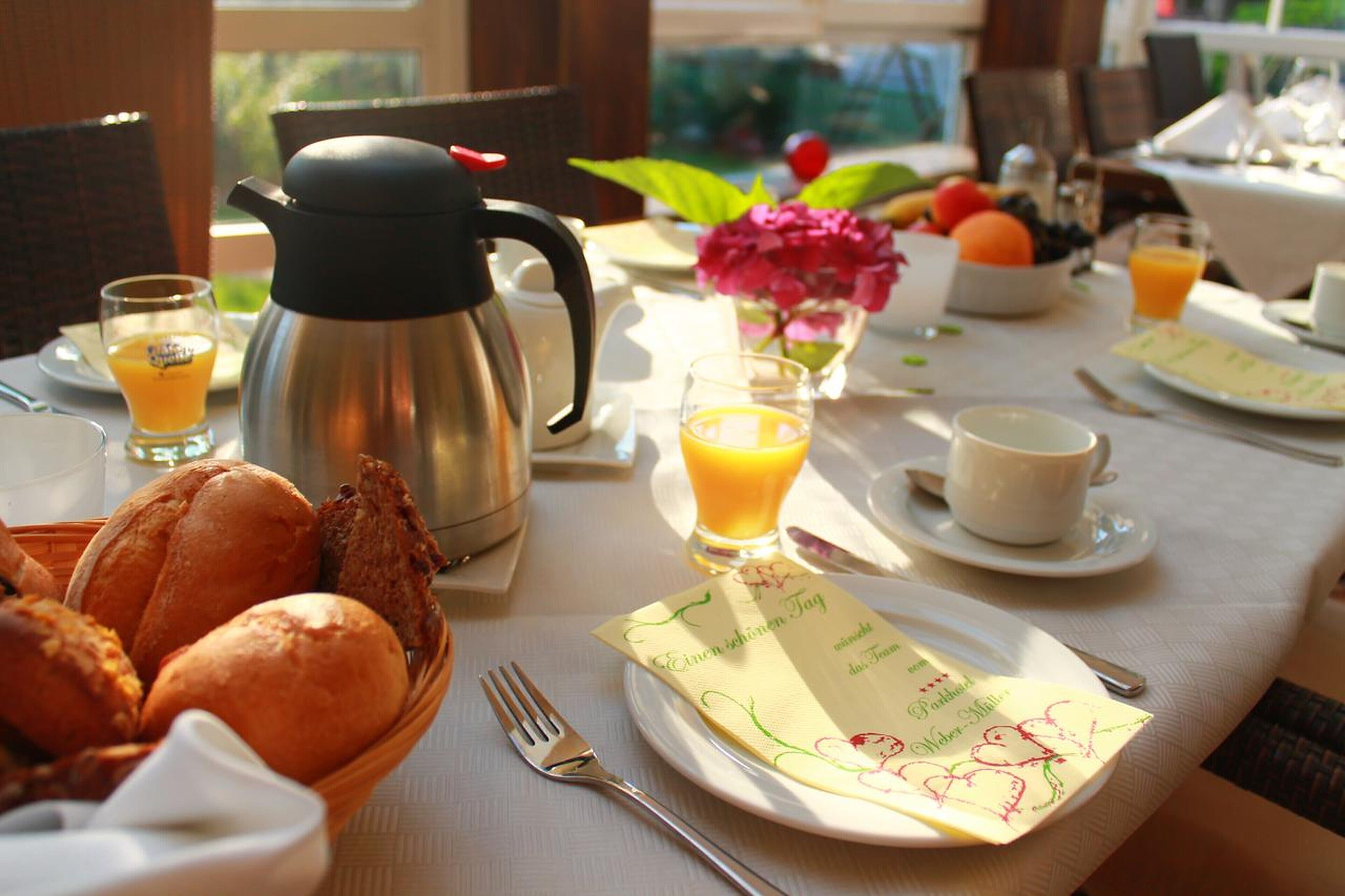 A breakfast table with a coffee pot, bread, fruit, and a menu.